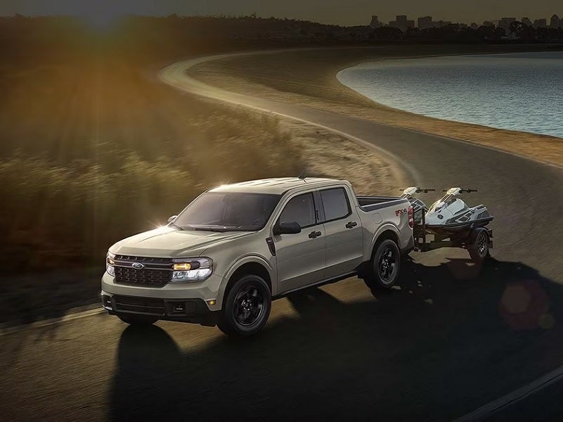 Ford Maverick hauling a pair of jet skis down a coastal road